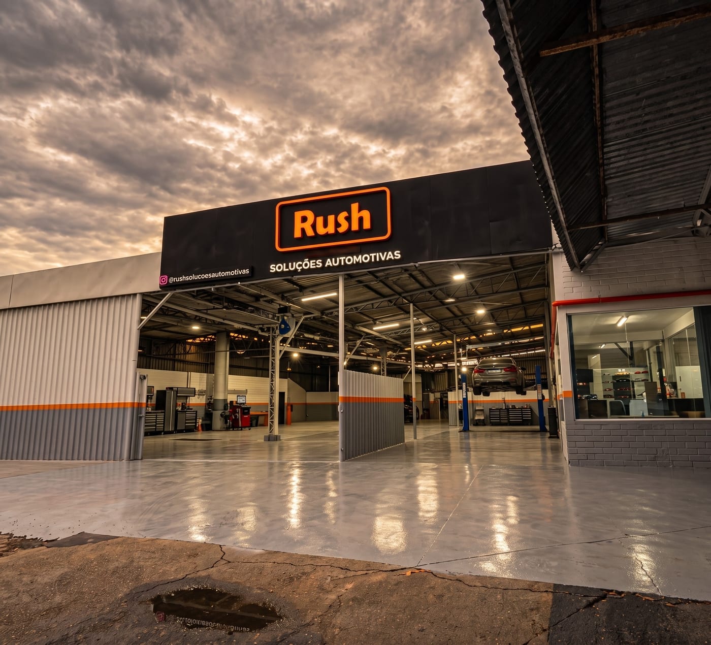 Fachada iluminada da Rush Car Barreiros ao entardecer, com a oficina ao fundo